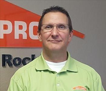 Male employee wearing a green SERVPRO shirt standing in front of a SERVPRO sign