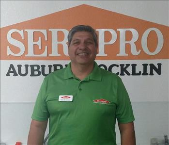 Male employee wearing a green SERVPRO shirt standing in front of a SERVPRO sign
